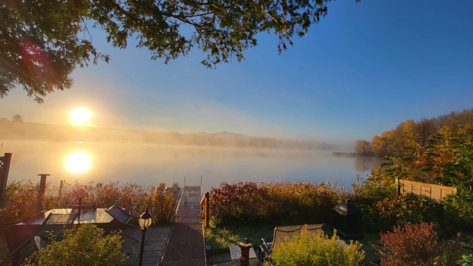 Une vue paisible sur un lac, avec une atmosphère brumeuse, un sentier menant à un quai et une végétation luxuriante tout autour.