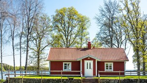 Una casa de madera roja con una puerta blanca, rodeada por un muro de piedra y una valla de madera.