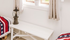 Una habitación con ventana, un banco, una mesa, una planta en maceta y un farol.