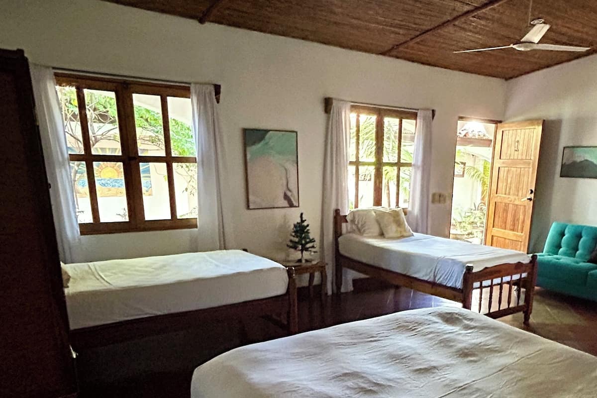 Habitación con dos camas individuales, ventilador de techo y vistas al exterior.