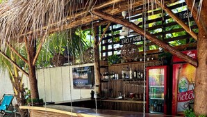 Een houten barruimte met een zitzet met schommel, een bordje met 'Hotel Tranquilo' en een koelkast vol drankjes.