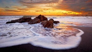 Een strand met grote rotsen en golven in de zonsondergang.