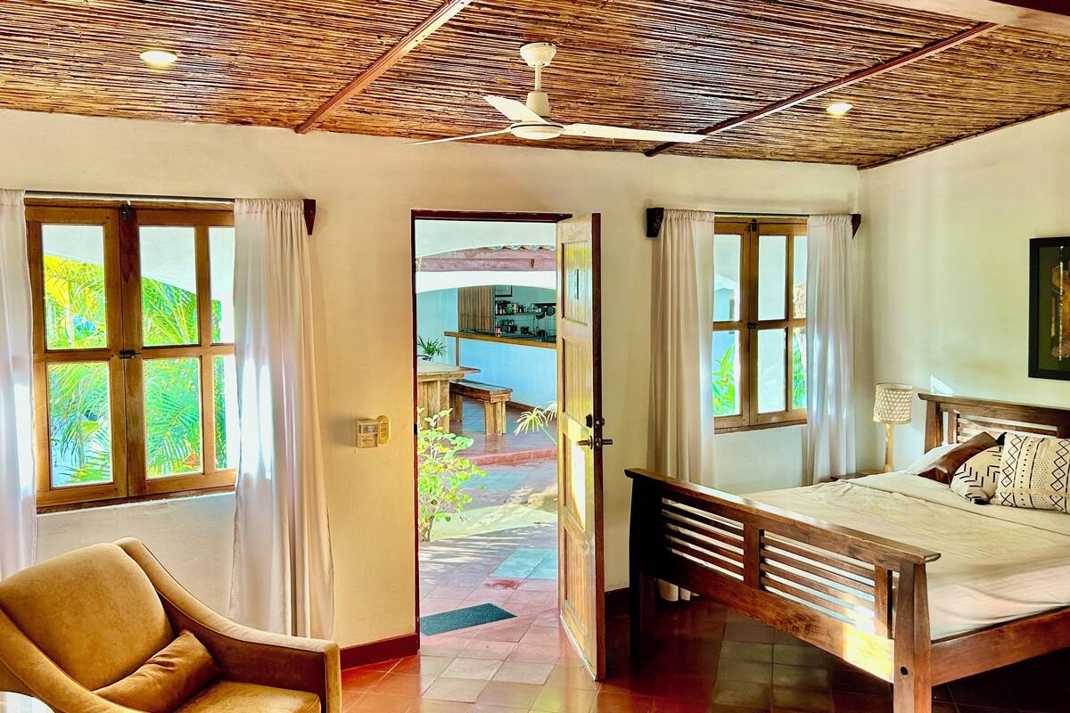 Una habitación con cama, una silla y vistas a una cocina y jardín a través de una puerta.