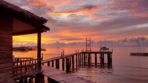 En träbrygga som sträcker sig ut i stilla vatten, med en solnedgång i bakgrunden.