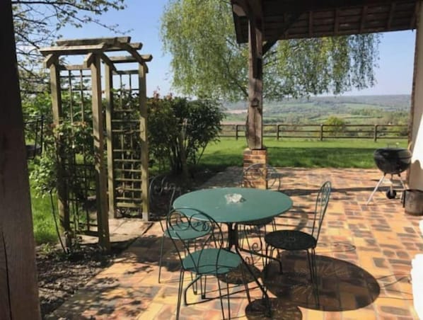 Una terrazza esterna con tavolo e sedie, un pergolato in legno e vista sulla campagna.