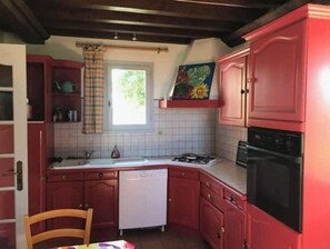 Una cucina compatta con mobili rossi, una lavastoviglie bianca, un fornello e una finestra con tenda.