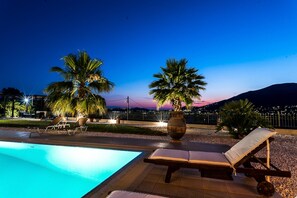 A pool area with lounge chairs and palm trees at dusk. - East Coast Mansion by Unique Villas Collection (Saronikos)