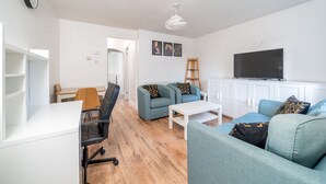 A modern living room with a white desk, a blue sofa, a white coffee table, and a TV mounted on the wall. - Crawley Pet Friendly 1-Bedroom Apartment (Crawley)