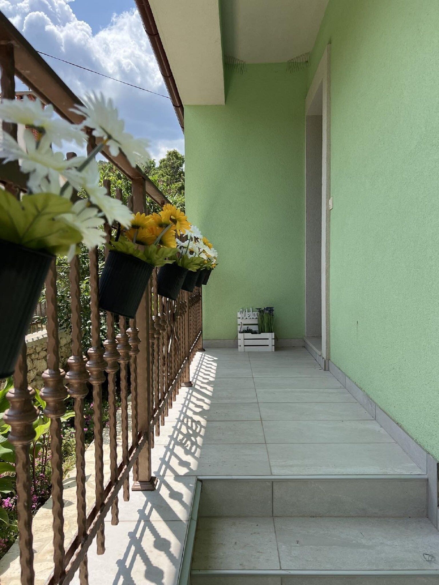 A balcony with a green wall, wooden railing, and potted plants.