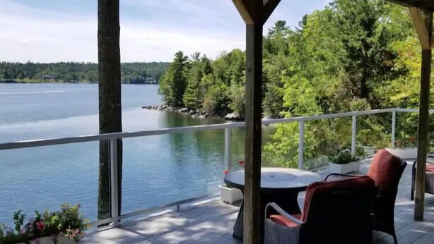 A covered outdoor deck with a view of a lake and forest.