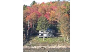 A lakeside cabin with a dock, surrounded by autumn-colored trees.