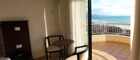 A balcony with a view of the ocean, a small table, two chairs, and a wooden cabinet.