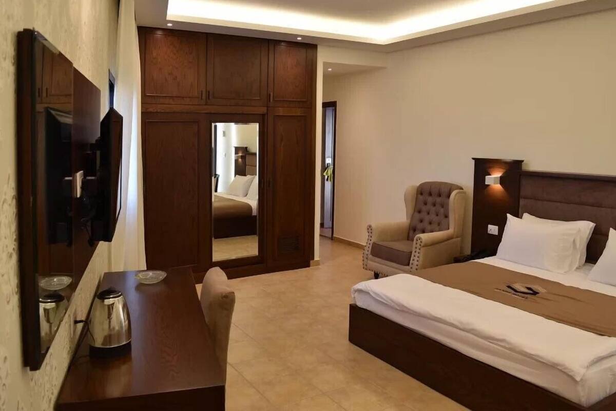 A hotel room with a bed, a desk, a chair, a TV, and a wardrobe.