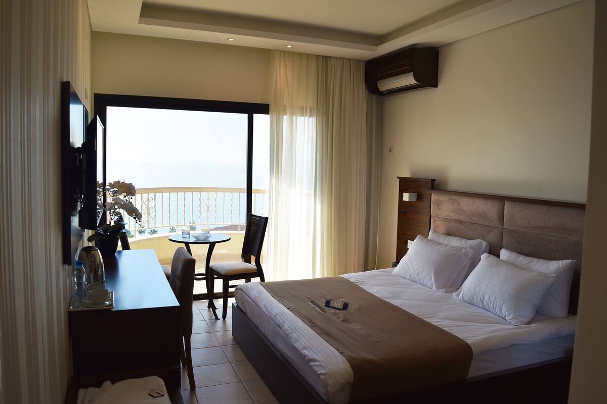 A hotel room with a bed, a desk, a chair, and a balcony with a view.