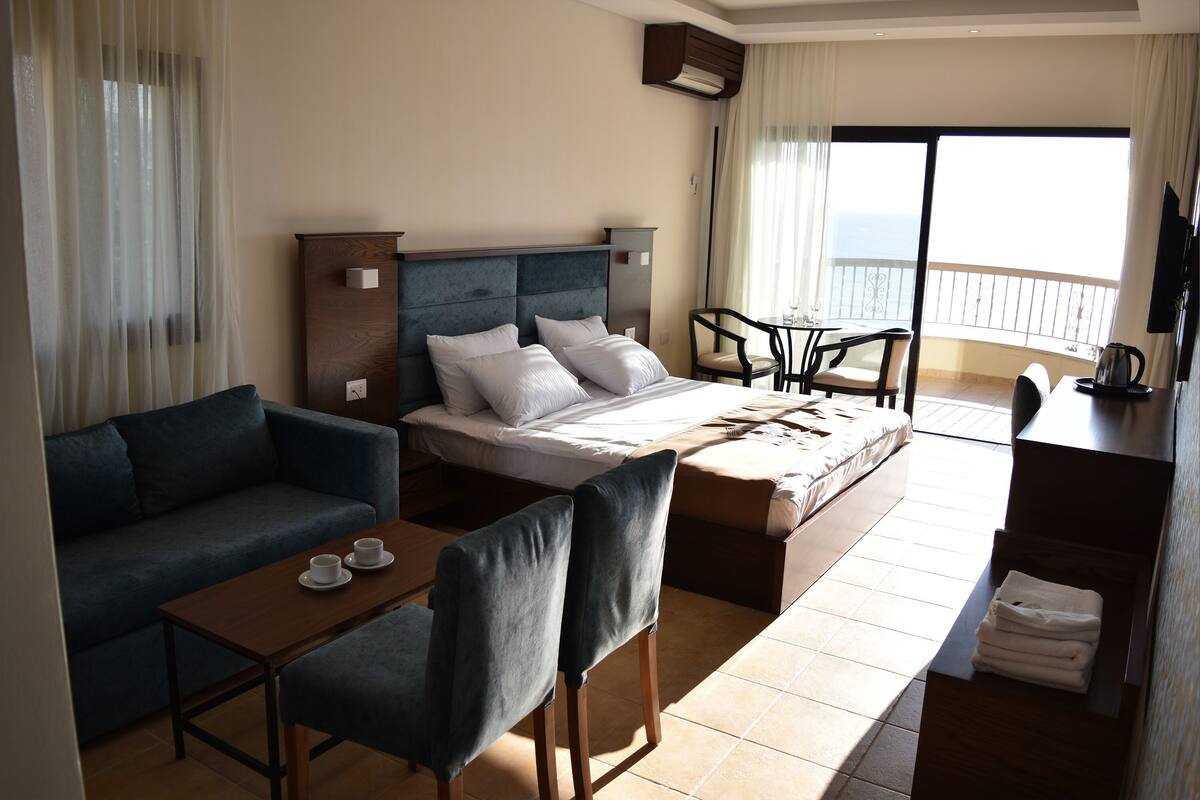 A hotel room with a bed, a sofa, a desk, and a balcony with a view.