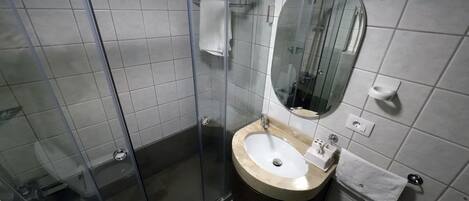 A bathroom with a glass-enclosed shower, a sink with a mirror, and tiled walls.
