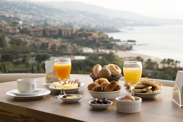 Ein Esstisch mit Croissants, Eiern und Orangensaft, mit Blick auf eine Küstenstadt.