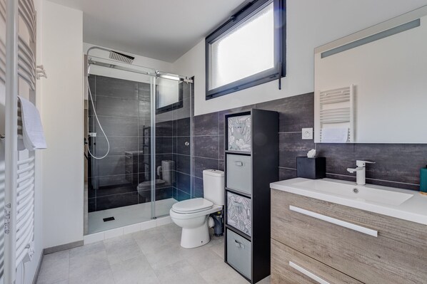 Uma casa de banho moderna com chuveiro envidraçado, sanita e toucador com espelho.
