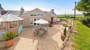 Una casa con un patio que cuenta con una mesa, sillas, una casita de juegos y un jardín.