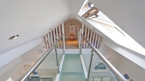 Una escalera con paredes de vidrio que conduce a un dormitorio en el segundo piso con tragaluces.
