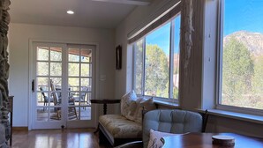 Amplia habitación con piso de madera, un ventanal con vista a árboles, un sofá y una mesa de comedor.