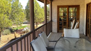 Un patio techado al aire libre con una mesa y sillas, vistas a árboles y un jardín, y una puerta de madera.