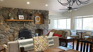 Una sala de estar acogedora con chimenea de piedra, una araña y un comedor con sillas y mesa de madera.