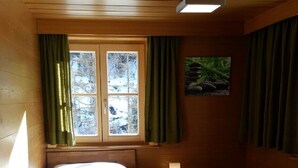 A wooden cabin bedroom with a bed, a nightstand, a window with curtains, and a wall-mounted picture. - Beautiful apartment on the 1st floor Top1 (Wald am Arlberg)