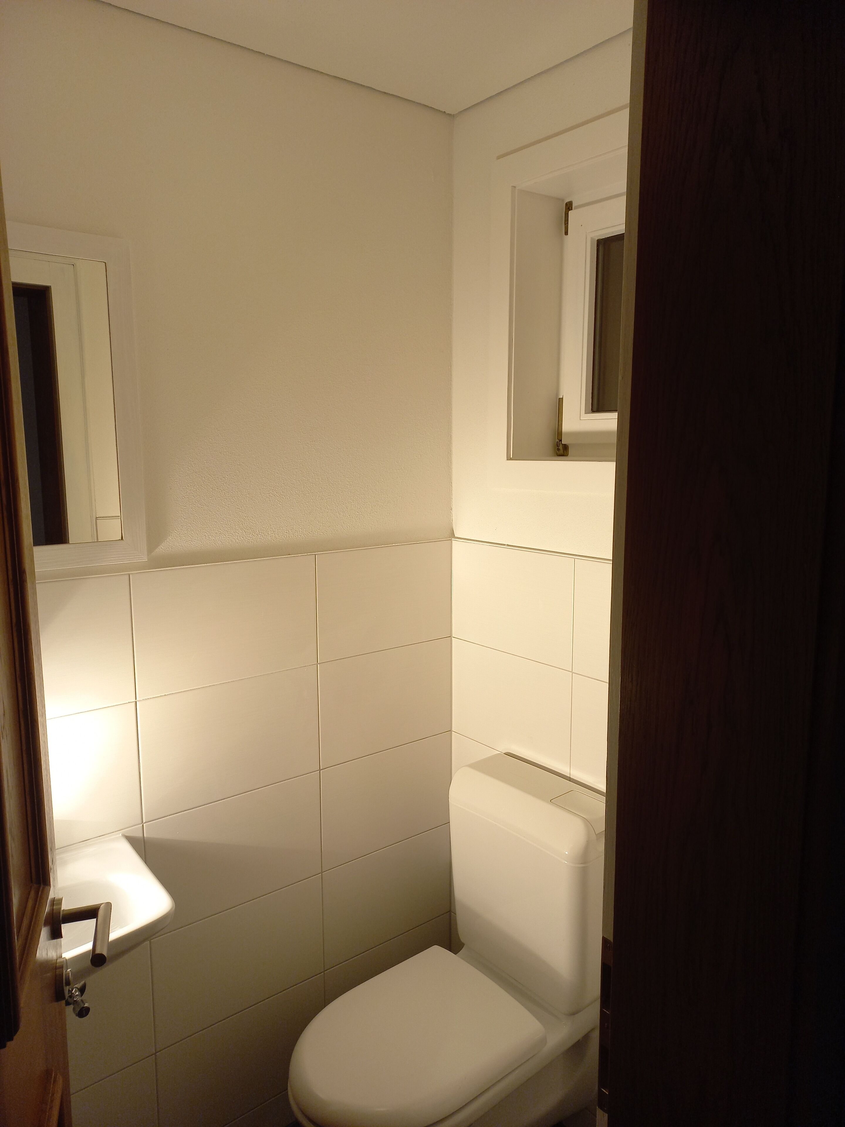 Ein kleines, weißes Badezimmer mit Toilette, Waschbecken und Spiegel.