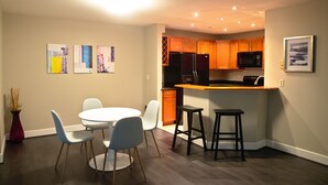 A modern kitchen with wooden cabinets, a black refrigerator, and a microwave. There is a dining area with a white table and blue chairs. - Spacious condo in downtown Bellevue (Bellevue)