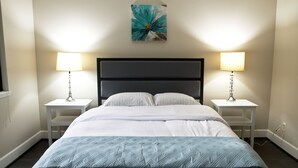 A neatly made bed with a quilted cover, two bedside tables with lamps, and a wall-mounted artwork above the bed. - Spacious condo in downtown Bellevue (Bellevue)