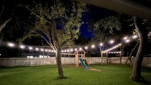 A backyard with a wooden play structure, a slide, and string lights.