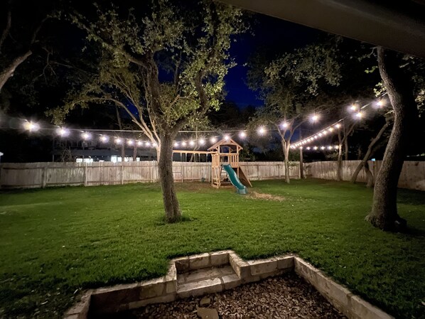 Ein Garten mit einer hölzernen Spielanlage, einer Rutsche und Lichterketten.