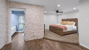 A bedroom with a stone accent wall, a wooden bed, and a ceiling fan.