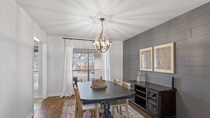 A dining area with a dark wooden table, white curtains, and a chandelier.