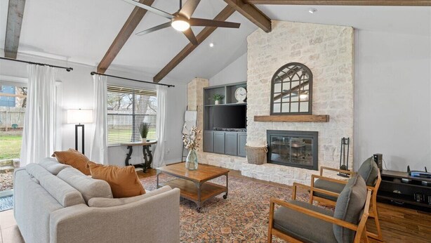 A living room with a stone fireplace, a television, and a ceiling fan.