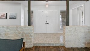 A room with a stone wall, a wooden floor, a white door, and a ceiling light.