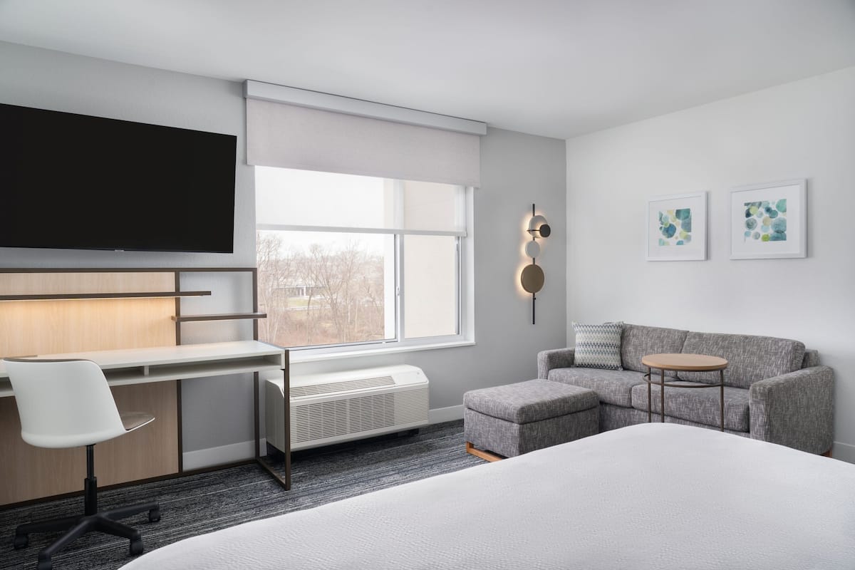 Une chambre d’hôtel moderne dotée d’un grand lit, d’un bureau avec une chaise, d’un canapé, d’une petite table et d’un téléviseur fixé au mur.