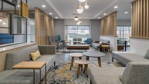 A modern lounge area with sofas, tables, and a large window providing a view of the outside. - Towneplace Suites By Marriott New Philadelphia (New Philadelphia)