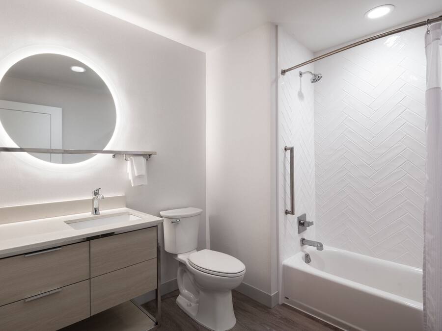 A modern bathroom with a round mirror, a toilet, a sink, and a bathtub.