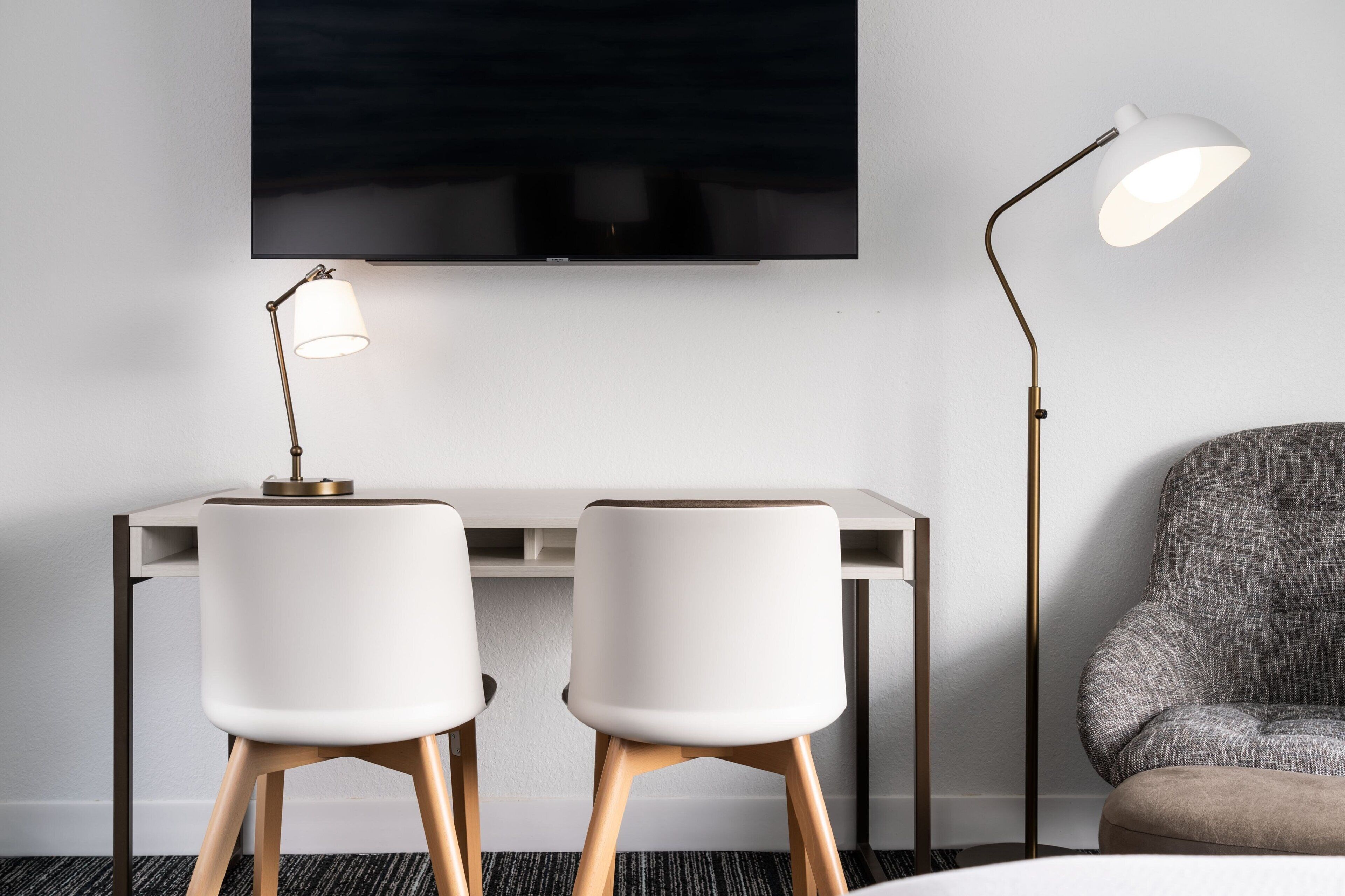 Una habitación moderna con un escritorio, dos sillas blancas, un televisor y dos lámparas de pie.