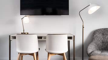 Una habitación moderna con un escritorio, dos sillas blancas, un televisor y dos lámparas de pie.