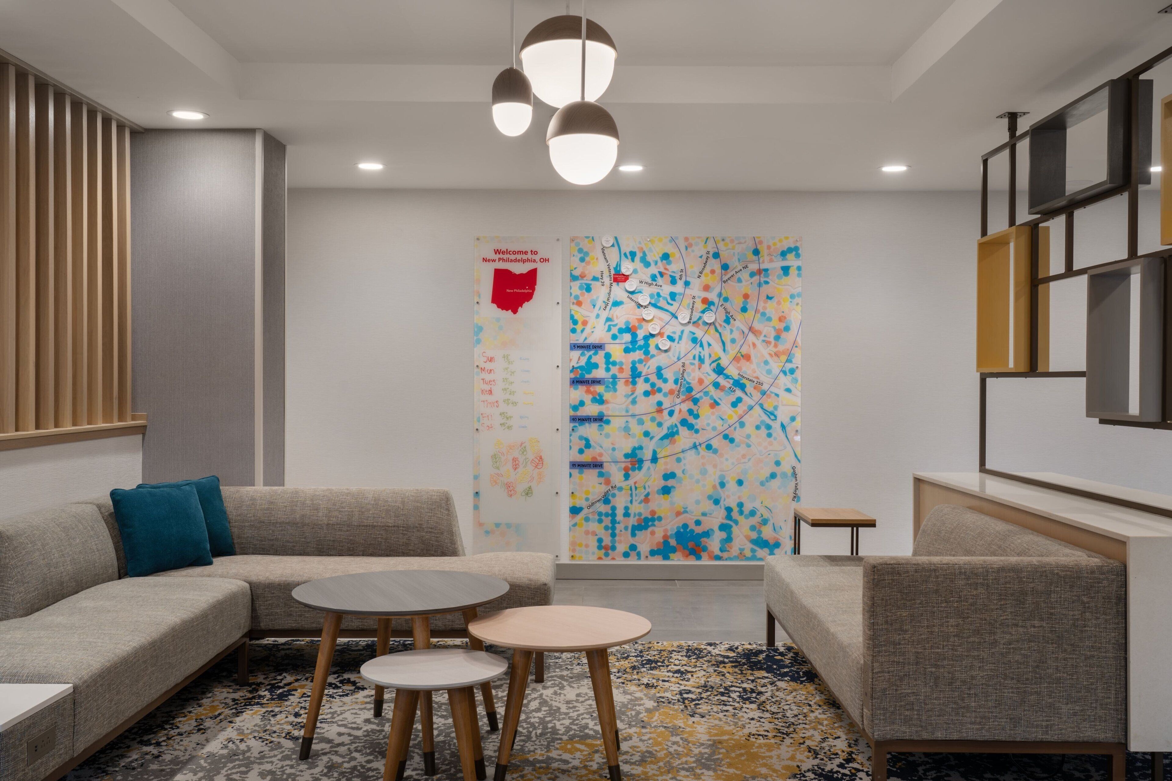 A modern hotel lobby with a sectional sofa, round tables, and a colorful abstract wall art.