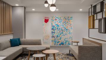 A modern hotel lobby with a sectional sofa, round tables, and a colorful abstract wall art.