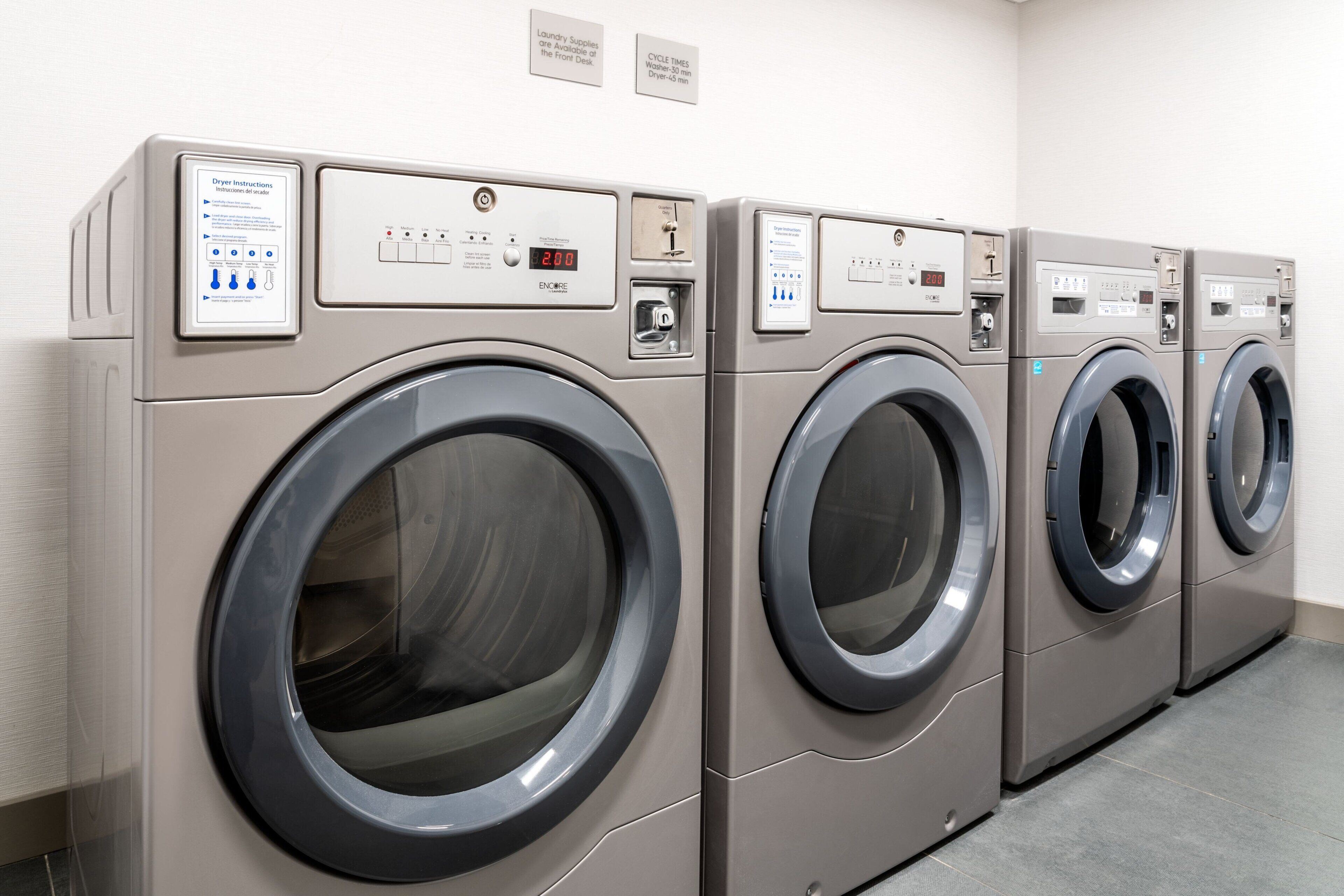 A row of four identical front-loading washing machines in a commercial laundry room.