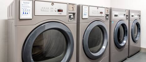 A row of four identical front-loading washing machines in a commercial laundry room.