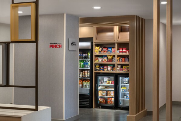 Un vestíbulo de hotel con una nevera portátil, un refrigerador lleno de aperitivos y un cartel que indica la ubicación de la nevera portátil.