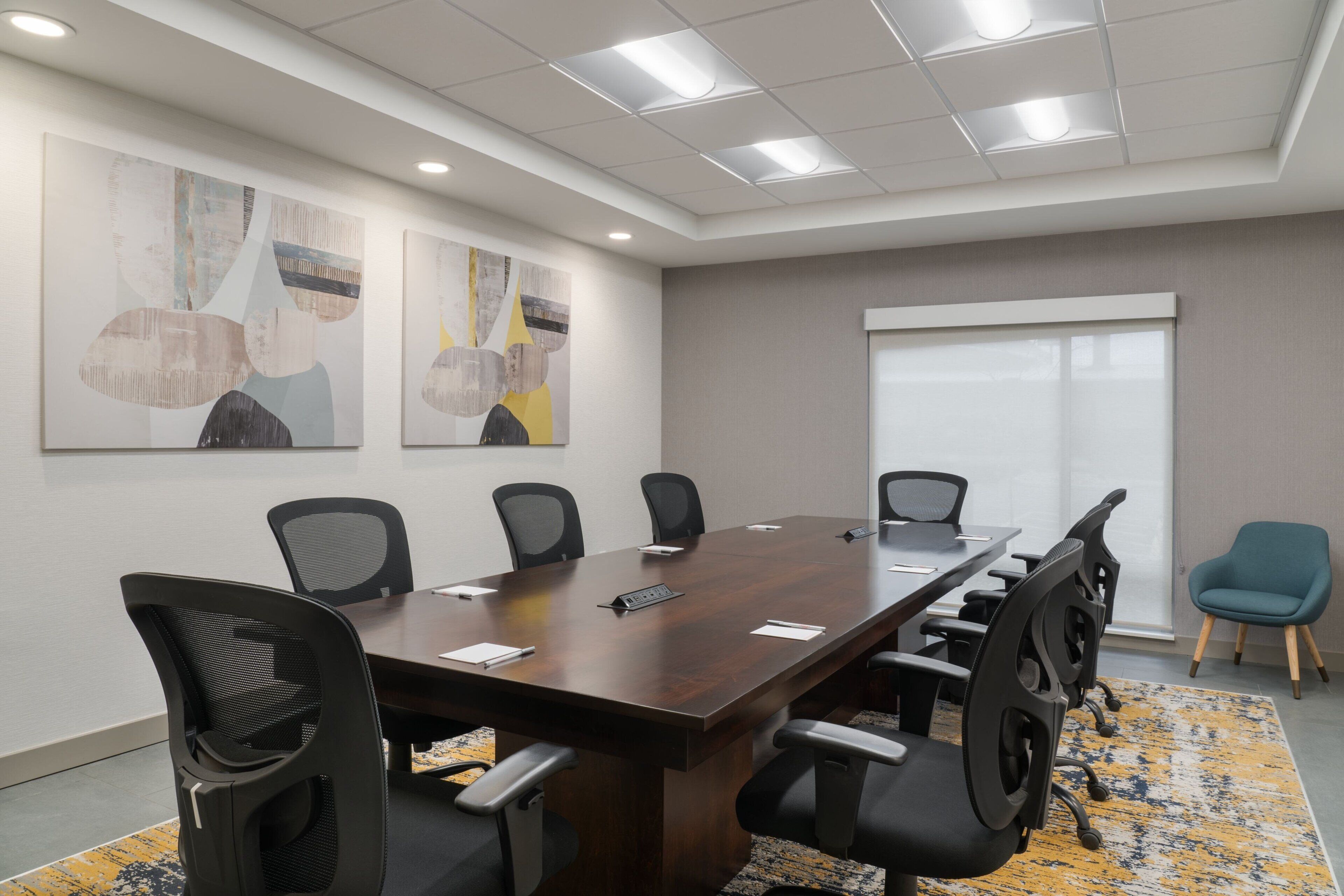 Una sala conferenze con un lungo tavolo, sei sedie e due dipinti astratti alle pareti.