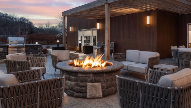 An outdoor patio area with a stone fire pit, wicker furniture, and a covered seating area. - Towneplace Suites By Marriott New Philadelphia (New Philadelphia)