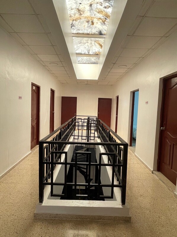 A corridor with a skylight, wooden doors, and a central black railing structure.
